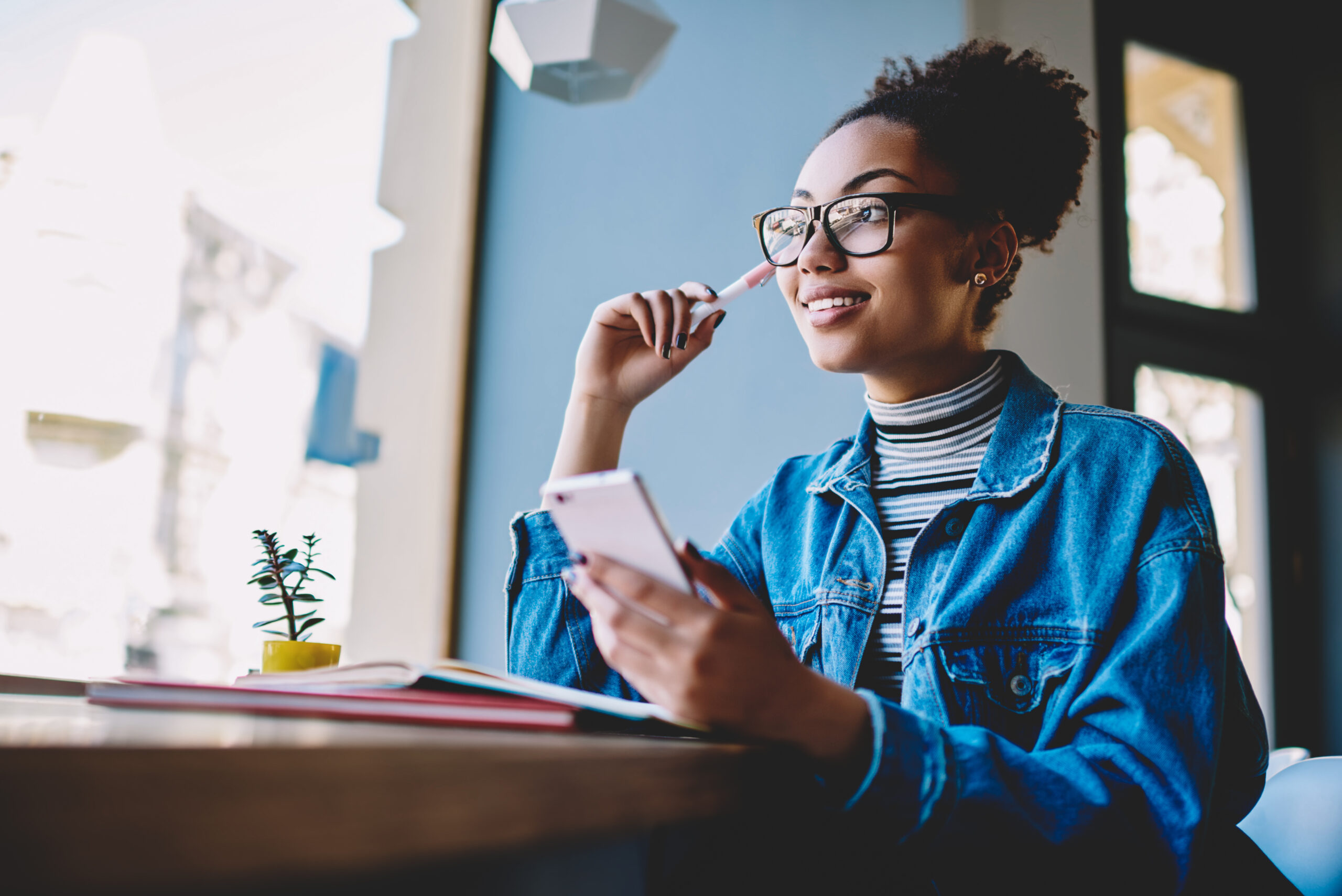 A woman wearing glasses sits with a textbook, looking into the distance while thinking about her Word of the Year during a study break.