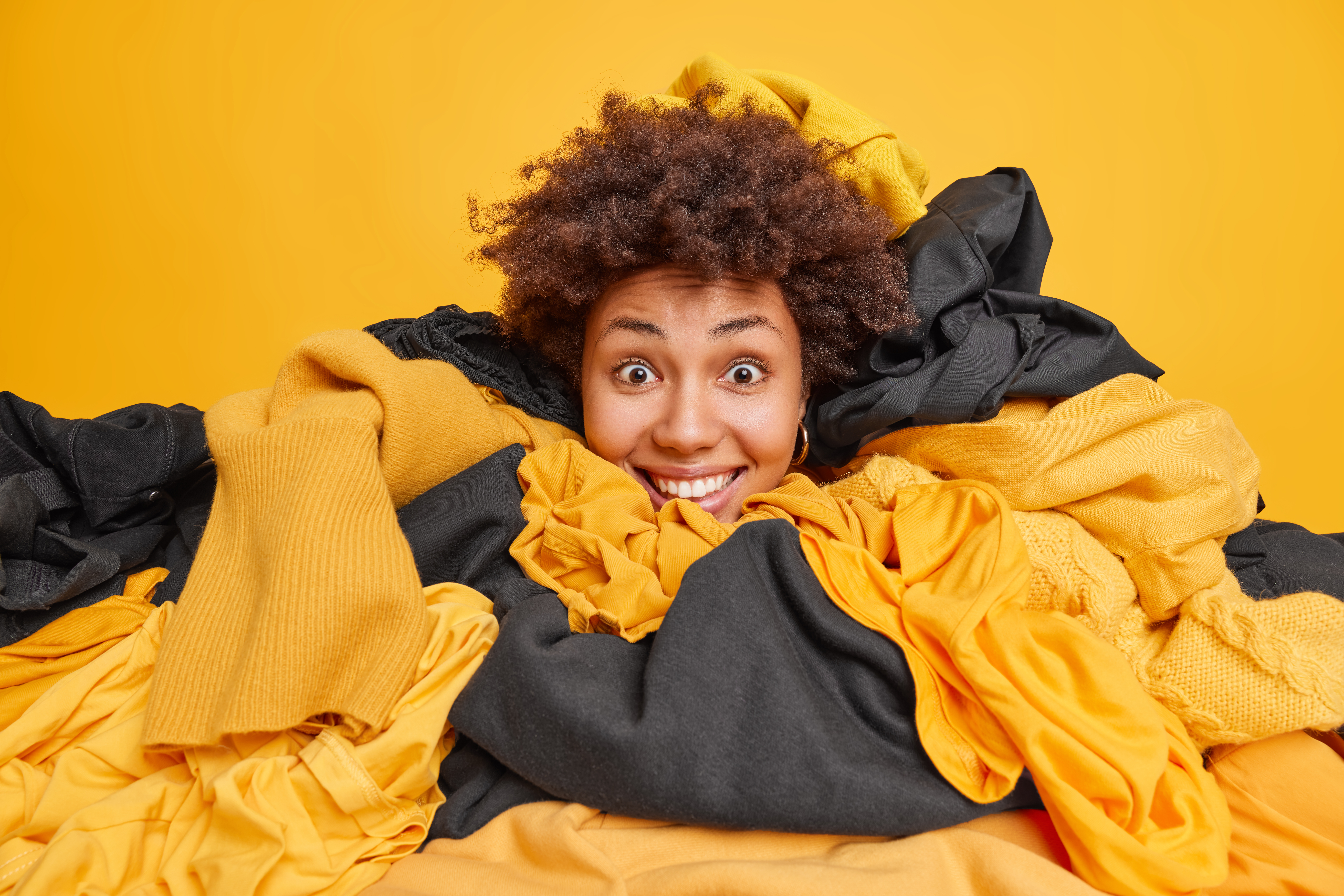 Student smiling while surrounded by a pile of yellow and black clothes, symbolizing spring cleaning and decluttering in student accommodation.